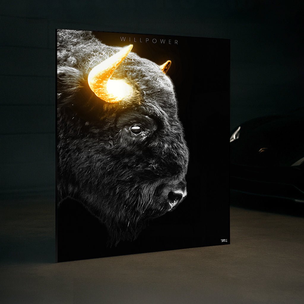 Framed ‘WILLPOWER’ fine art print of a powerful bison with glowing golden horns displayed in a high-end garage interior near a luxury car.